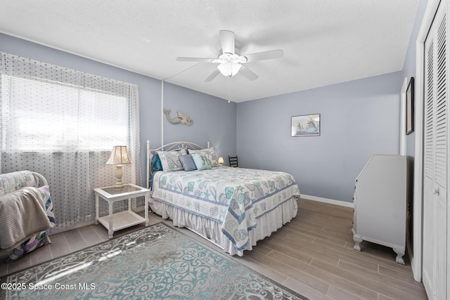 bedroom featuring a textured ceiling, a ceiling fan, baseboards, a closet, and wood tiled floor