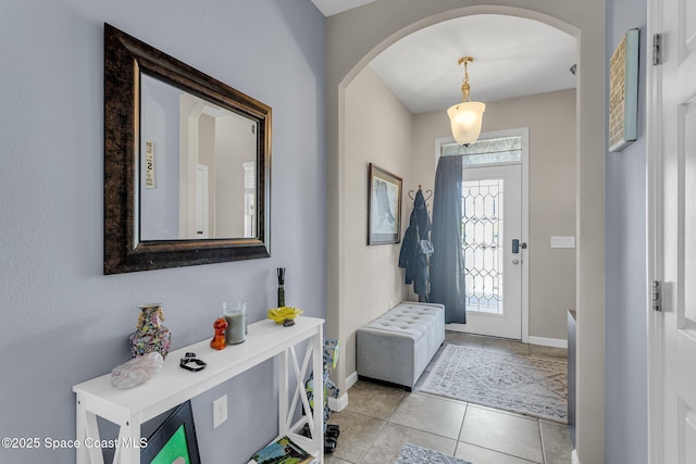 foyer entrance featuring baseboards, arched walkways, and light tile patterned flooring