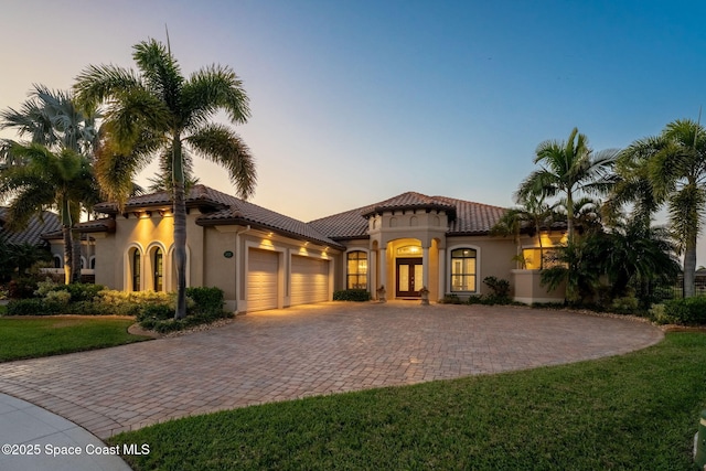 mediterranean / spanish house featuring a garage, stucco siding, a tile roof, and french doors