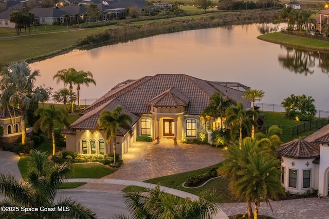 mediterranean / spanish-style home with a tile roof, decorative driveway, a water view, and stucco siding