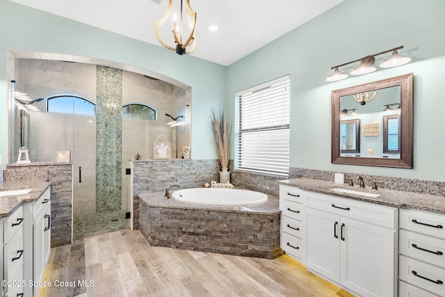 bathroom featuring two vanities, wood finished floors, a sink, a shower stall, and a bath