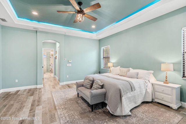 bedroom featuring arched walkways, baseboards, a raised ceiling, and light wood-style floors