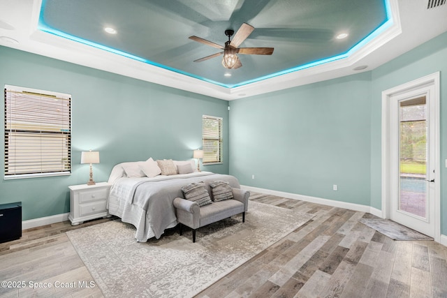 bedroom with access to exterior, light wood-style flooring, baseboards, and a raised ceiling