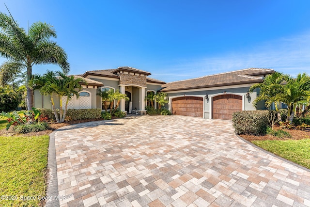 mediterranean / spanish home with an attached garage, a tile roof, decorative driveway, and stucco siding