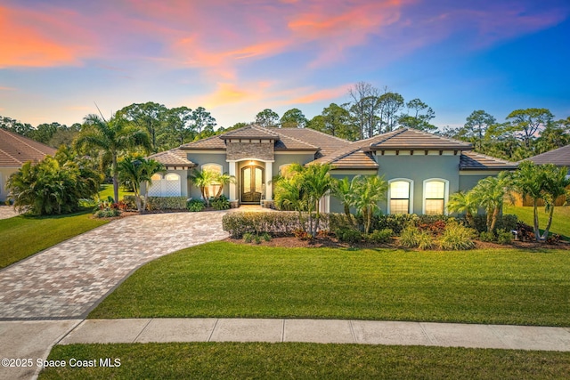 mediterranean / spanish home featuring a tiled roof, french doors, decorative driveway, a lawn, and stucco siding