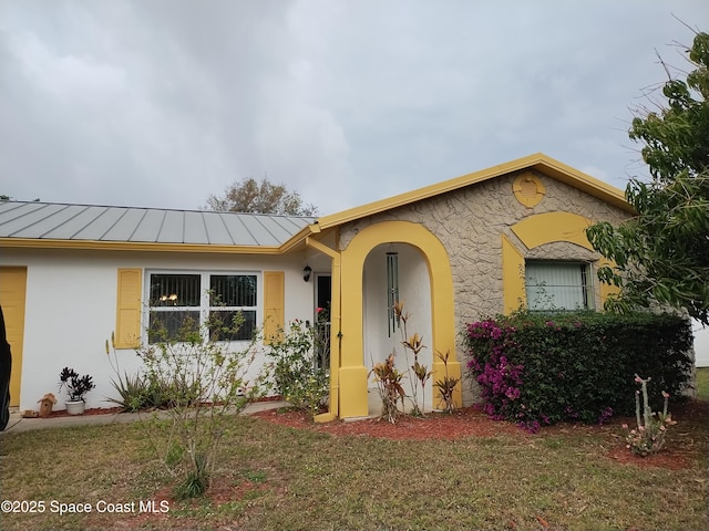 view of front facade with stucco siding, a front lawn, metal roof, and a standing seam roof