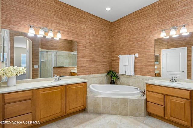 full bath with a stall shower, two vanities, a sink, and a bath