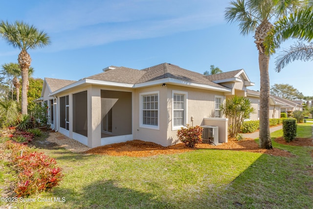 back of house with central AC unit, a sunroom, roof with shingles, a yard, and stucco siding