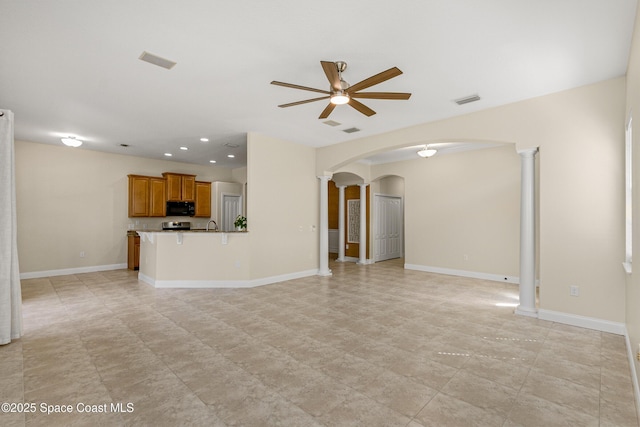 unfurnished living room featuring ornate columns, visible vents, arched walkways, and baseboards