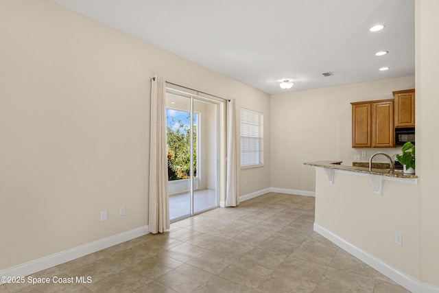 kitchen featuring a breakfast bar area, visible vents, brown cabinetry, dark stone countertops, and baseboards