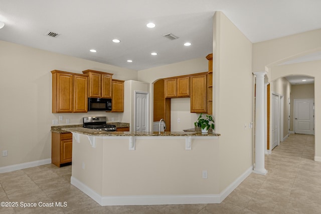 kitchen with arched walkways, visible vents, stainless steel gas range, dark stone counters, and black microwave