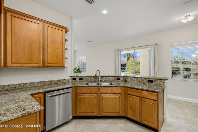 kitchen featuring stone countertops, a peninsula, a sink, brown cabinets, and dishwasher