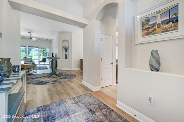 foyer with ceiling fan, baseboards, arched walkways, and wood finished floors