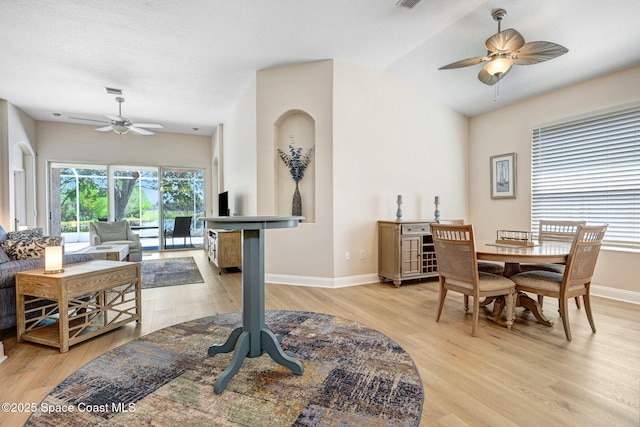 dining space with a ceiling fan, baseboards, visible vents, light wood-style flooring, and vaulted ceiling