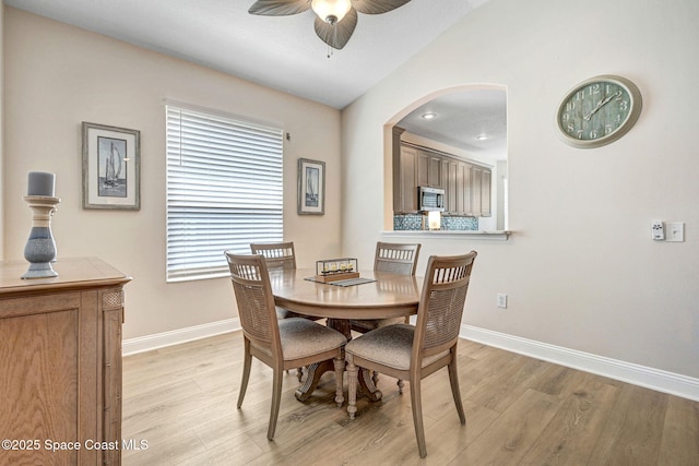 dining room featuring baseboards, light wood-style floors, ceiling fan, and arched walkways