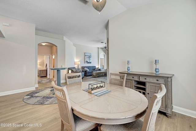 dining space with baseboards, arched walkways, light wood-style floors, and a ceiling fan