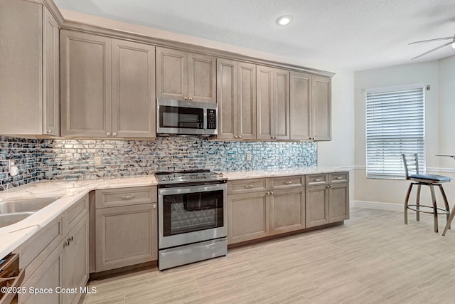 kitchen with light stone countertops, a sink, ceiling fan, appliances with stainless steel finishes, and tasteful backsplash