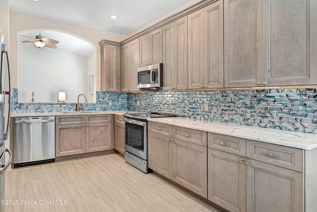 kitchen featuring backsplash, ceiling fan, light stone countertops, appliances with stainless steel finishes, and a sink