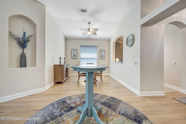 interior space featuring a ceiling fan, visible vents, baseboards, light wood finished floors, and arched walkways