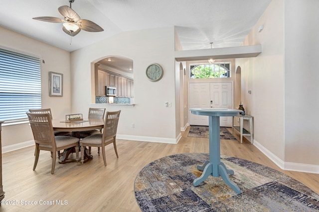 dining area with baseboards, light wood-type flooring, vaulted ceiling, arched walkways, and a ceiling fan