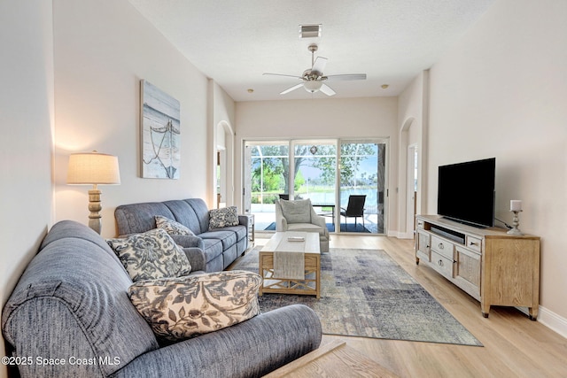 living area with visible vents, arched walkways, light wood-style floors, baseboards, and ceiling fan