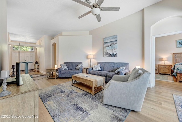 living area with a ceiling fan, arched walkways, light wood finished floors, and baseboards