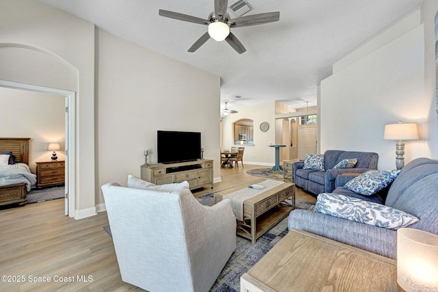 living room featuring a ceiling fan, baseboards, light wood finished floors, arched walkways, and a textured ceiling