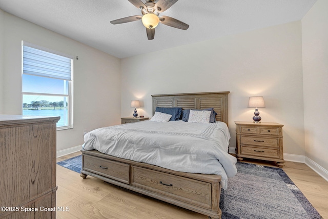 bedroom with a ceiling fan, light wood-type flooring, baseboards, and a water view