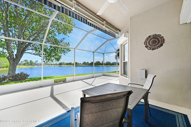 view of patio featuring glass enclosure, a water view, and a ceiling fan