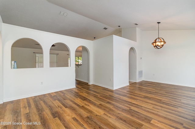 empty room with lofted ceiling, a notable chandelier, visible vents, and dark wood-style flooring