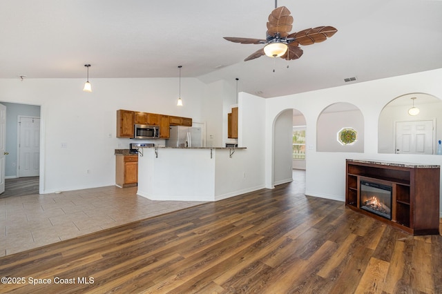 kitchen with appliances with stainless steel finishes, open floor plan, brown cabinetry, and decorative light fixtures