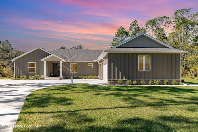 view of front facade with roof with shingles, an attached garage, board and batten siding, a front yard, and driveway