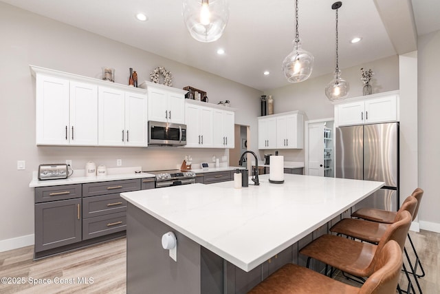 kitchen featuring gray cabinetry, white cabinetry, appliances with stainless steel finishes, a kitchen bar, and pendant lighting