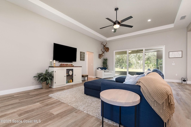 living room with light wood finished floors, a raised ceiling, visible vents, and baseboards