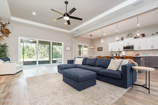 living area featuring light wood-type flooring, a raised ceiling, visible vents, and ceiling fan