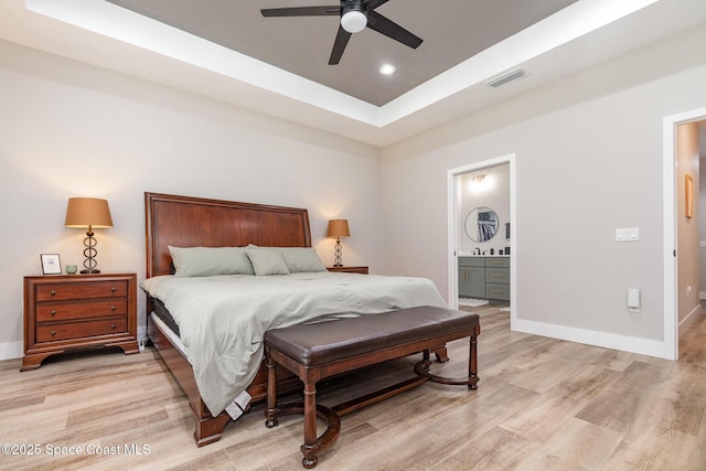 bedroom with a tray ceiling, light wood-style flooring, visible vents, and baseboards