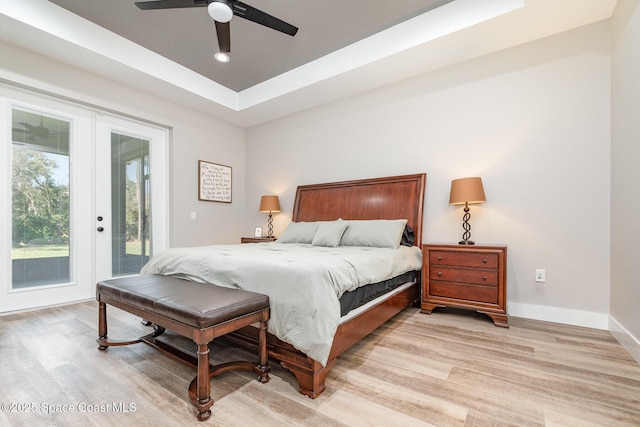 bedroom featuring access to exterior, baseboards, a raised ceiling, and light wood finished floors