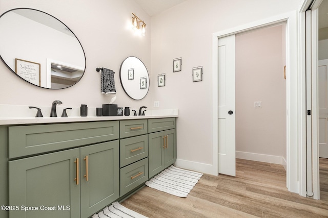 full bath with a sink, double vanity, wood finished floors, and baseboards