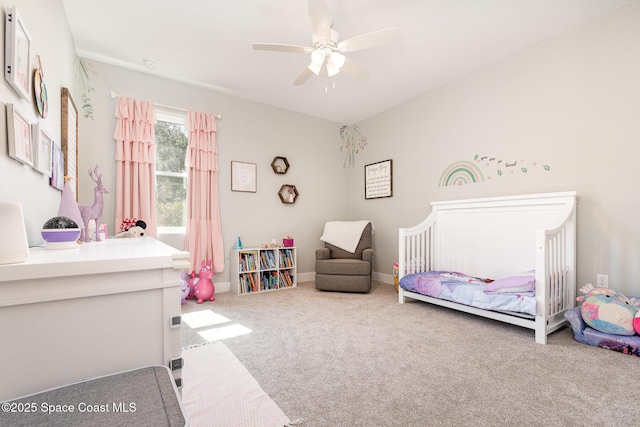 carpeted bedroom featuring a nursery area, a ceiling fan, and baseboards