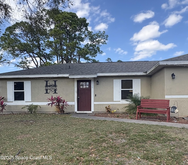 view of front of home with roof with shingles, a front yard, and stucco siding