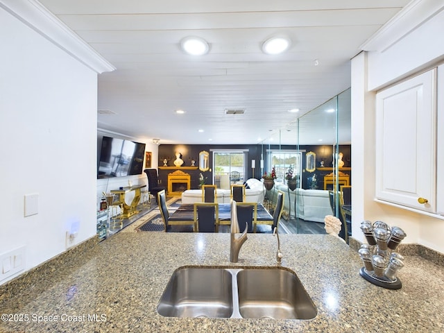 kitchen featuring dark stone countertops, white cabinetry, open floor plan, and a sink