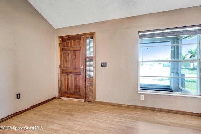 entrance foyer featuring light wood-type flooring, baseboards, a textured ceiling, and lofted ceiling