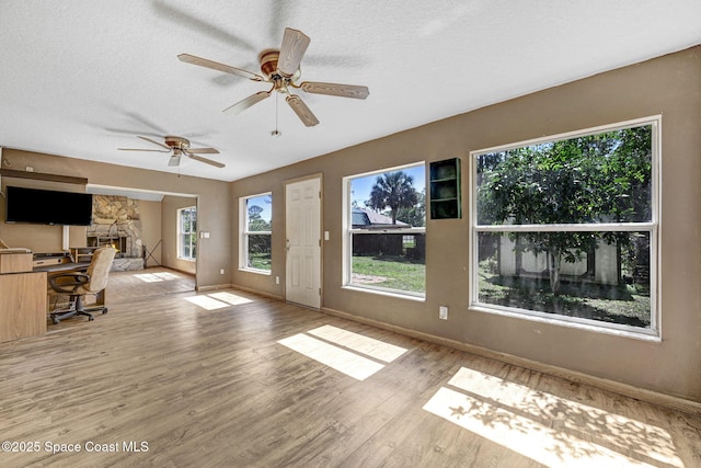 unfurnished living room with light wood-style floors, a fireplace, a textured ceiling, and baseboards