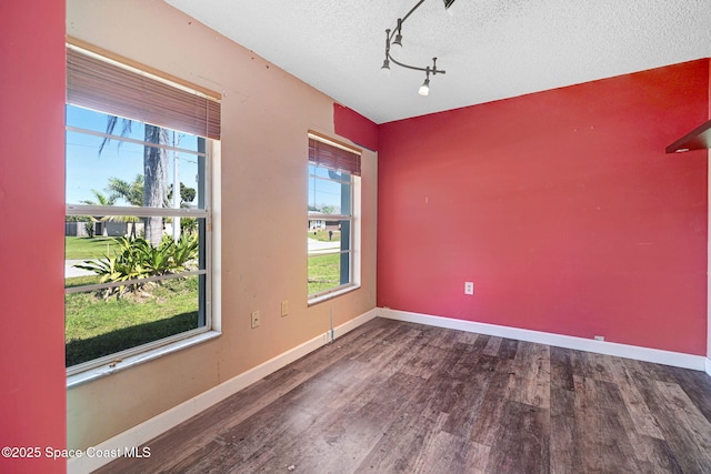 unfurnished room with track lighting, a textured ceiling, baseboards, and wood finished floors