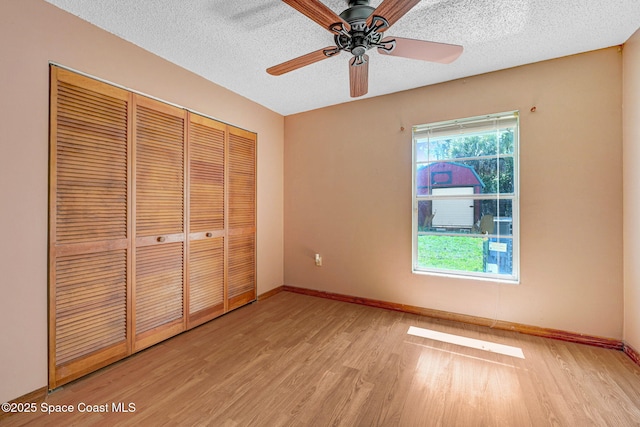 unfurnished bedroom featuring a closet, light wood-style flooring, baseboards, and a textured ceiling