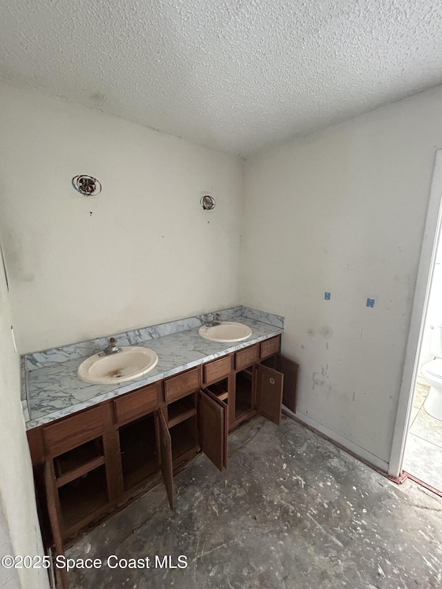 full bath with double vanity, a textured ceiling, and a sink