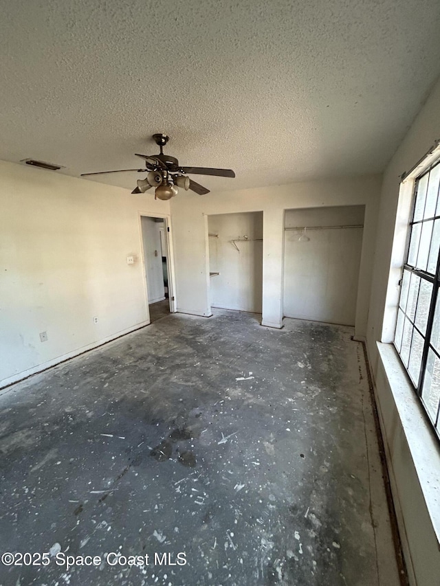 unfurnished bedroom with concrete flooring, a textured ceiling, two closets, and visible vents