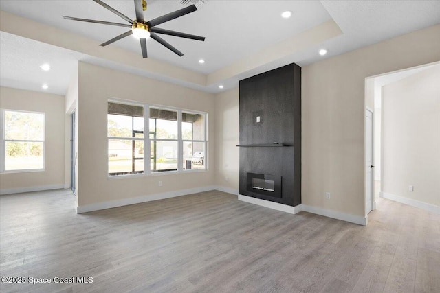 unfurnished living room with light wood-style flooring, a fireplace, baseboards, and a raised ceiling