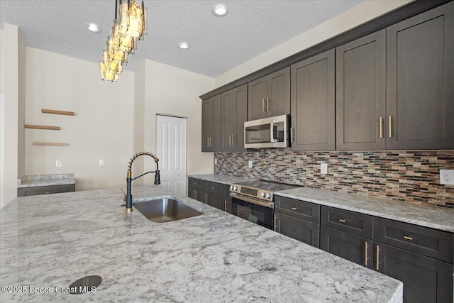 kitchen featuring light stone counters, stainless steel appliances, backsplash, a kitchen island with sink, and a sink