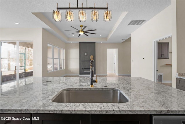 kitchen featuring a tray ceiling, open floor plan, a sink, and light stone countertops